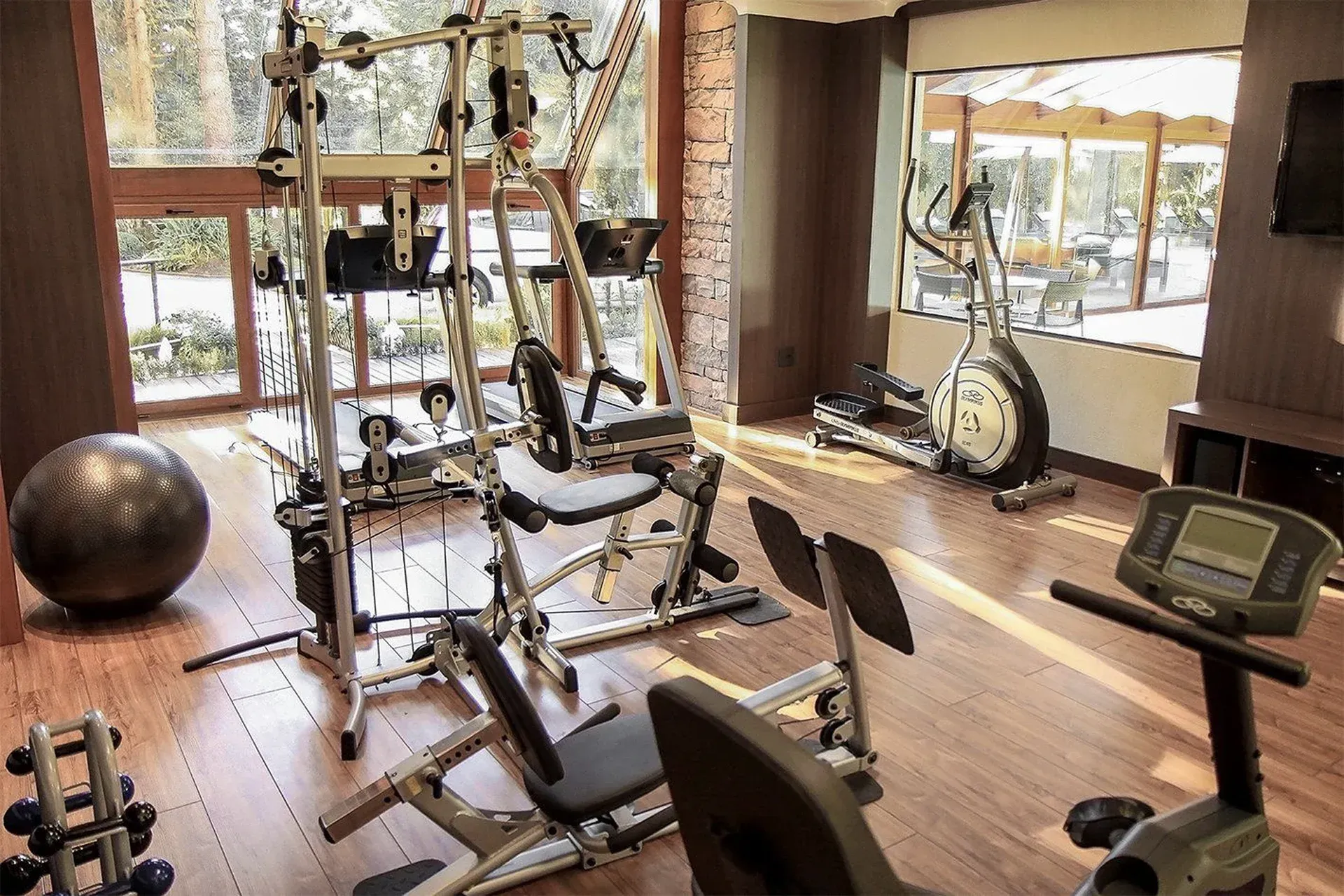 Academia em casa com aparelhos de ginástica, esteira e equipamentos de fitness junto a uma grande janela.