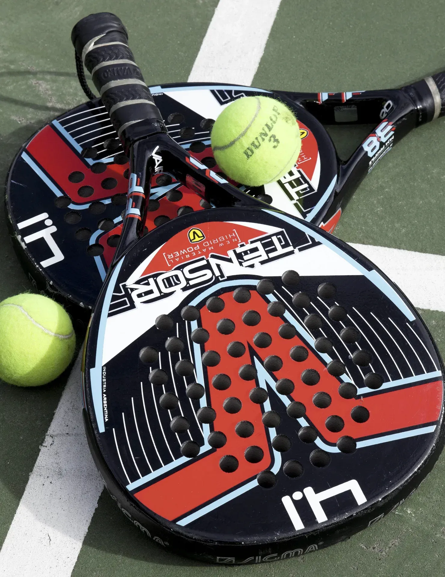 Duas raquetes de padel e bolas de tênis em uma quadra, com uma raquete em primeiro plano.