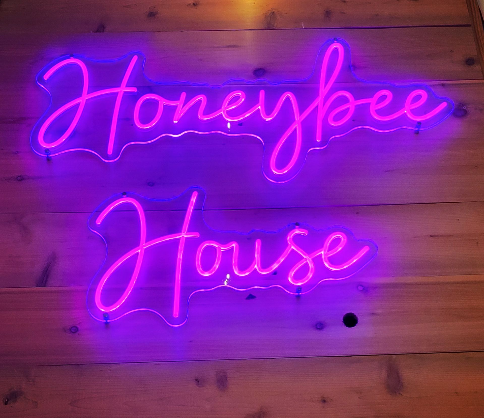 A neon sign that says honeybee house is on a wooden floor.