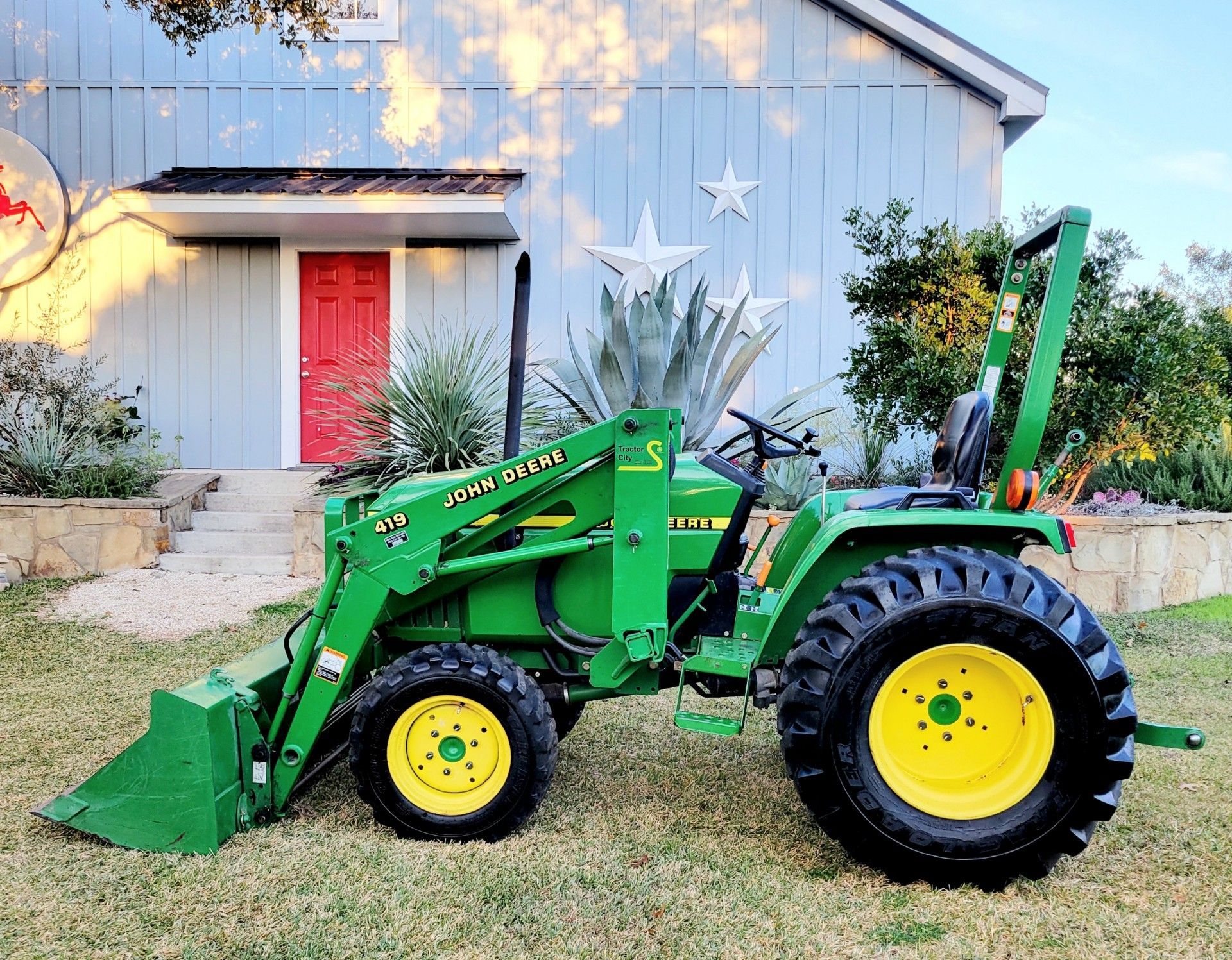 A green john deere tractor is parked in front of a house