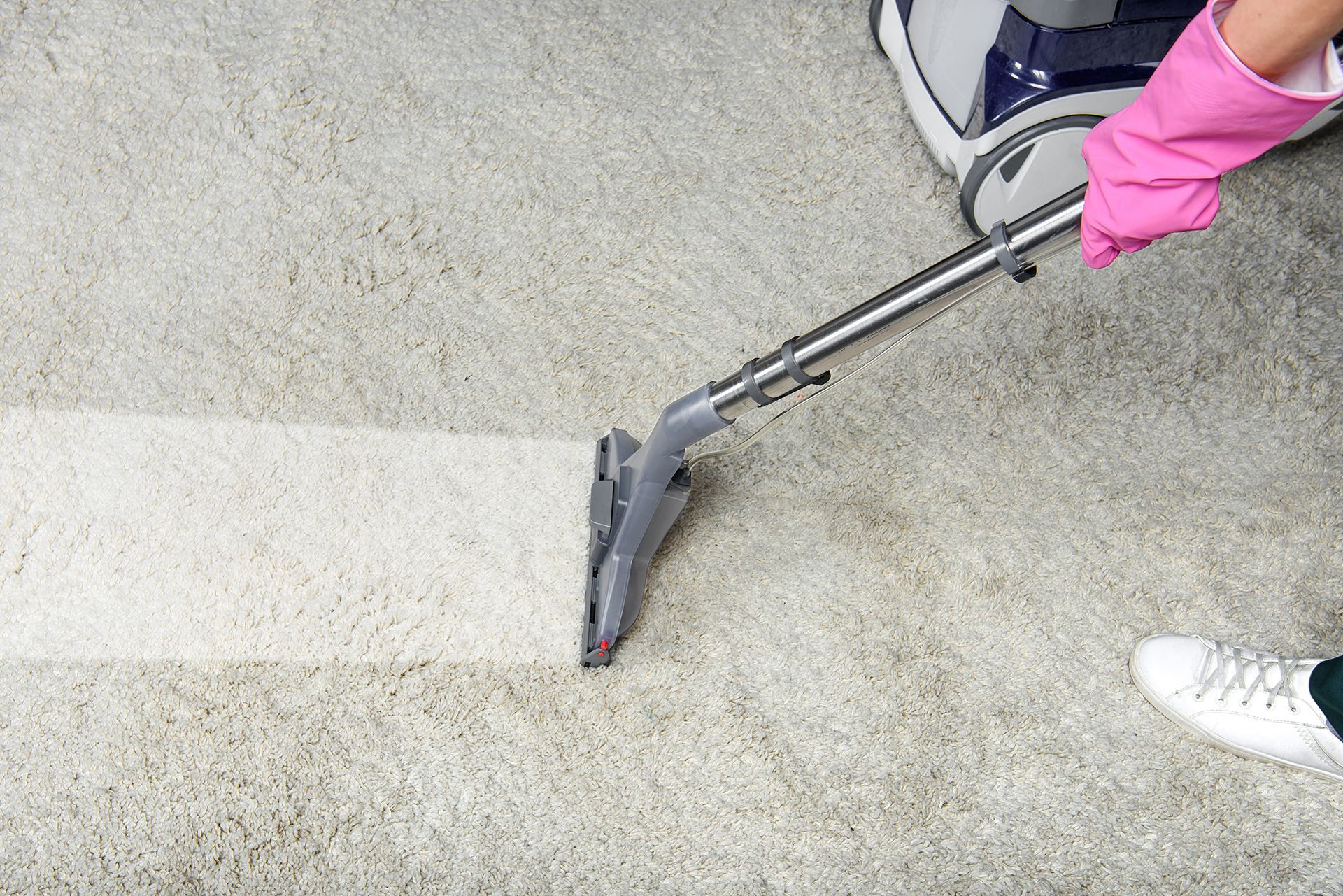 A person wearing pink gloves is using a vacuum cleaner to clean a carpet.