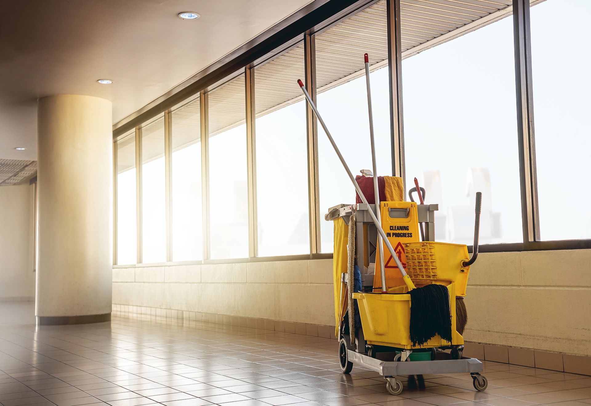 A yellow mop trolley is parked in a hallway next to a window.