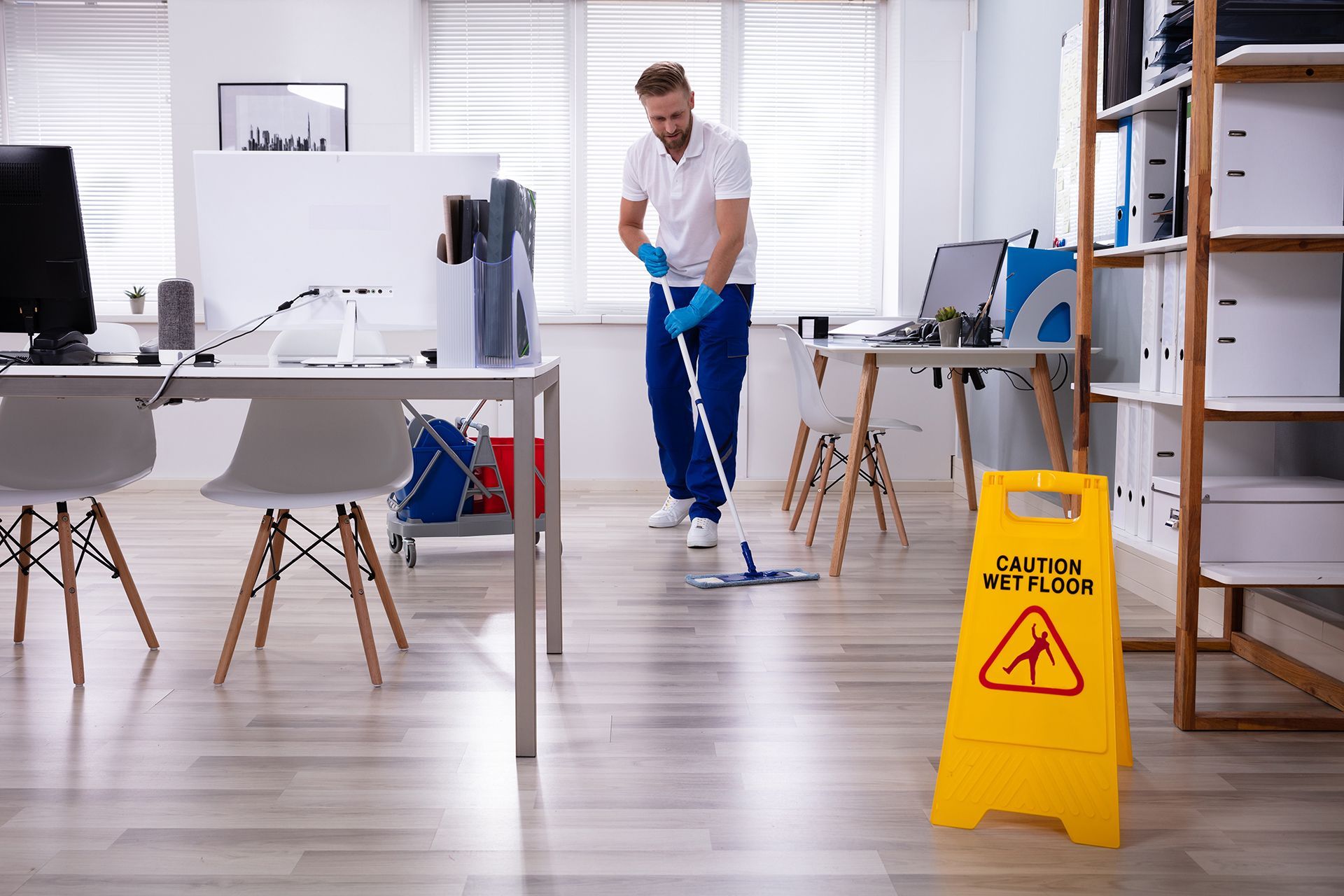 A man is mopping the floor of an office next to a caution sign.