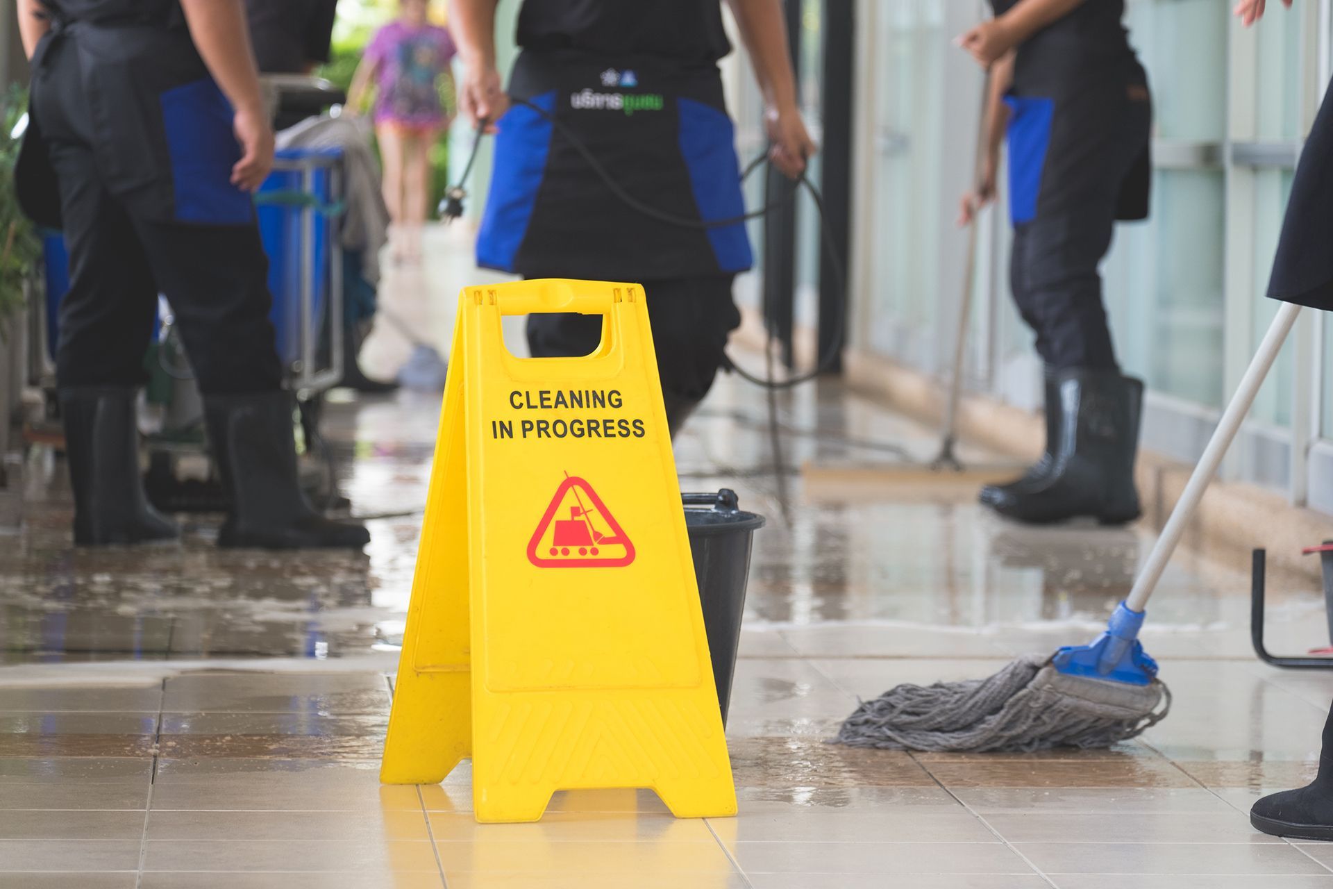 A group of cleaners are cleaning a floor with a yellow caution sign.