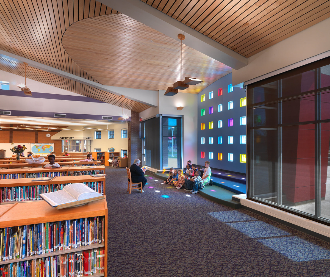 Library interior with bookshelves, children reading, colorful window, and patterned ceiling.