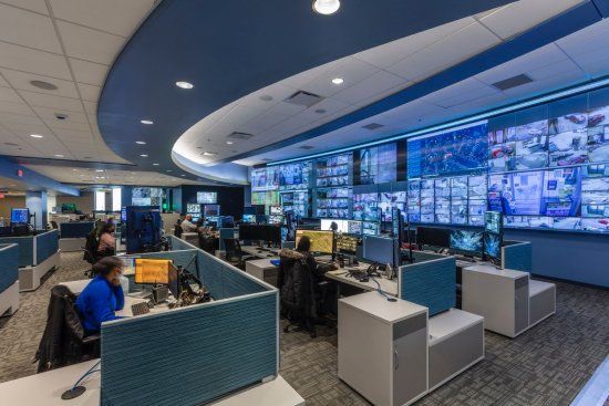 Control room with rows of monitors, people at workstations, and blue and white color scheme.