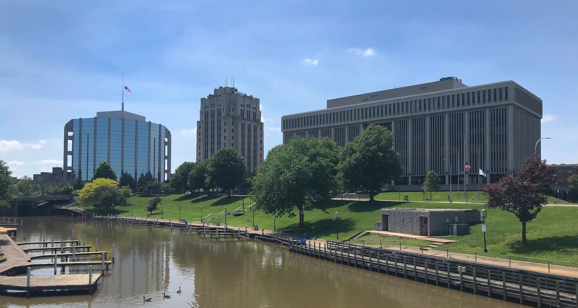 River scene with three buildings, trees, a boat dock, and a blue sky.
