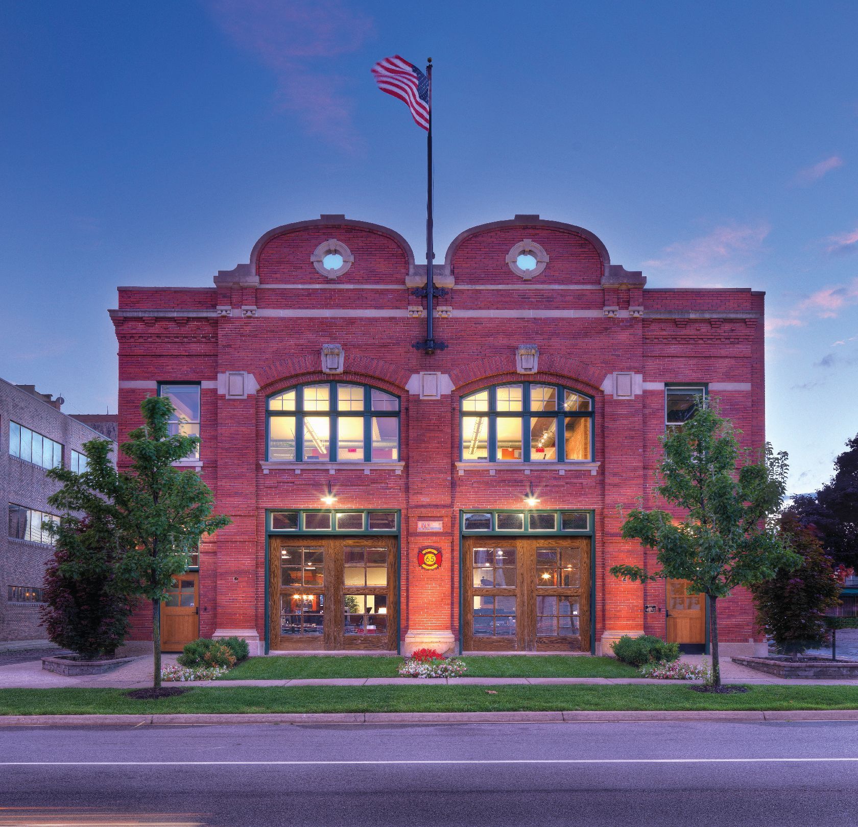Red brick building with arched windows and wooden doors, American flag on roof.