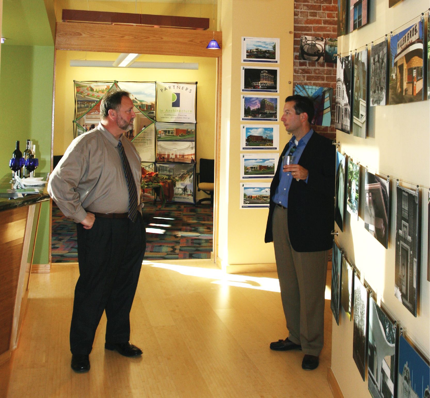 Two men in a gallery, viewing art on the walls. One wears a suit, the other a shirt and tie.