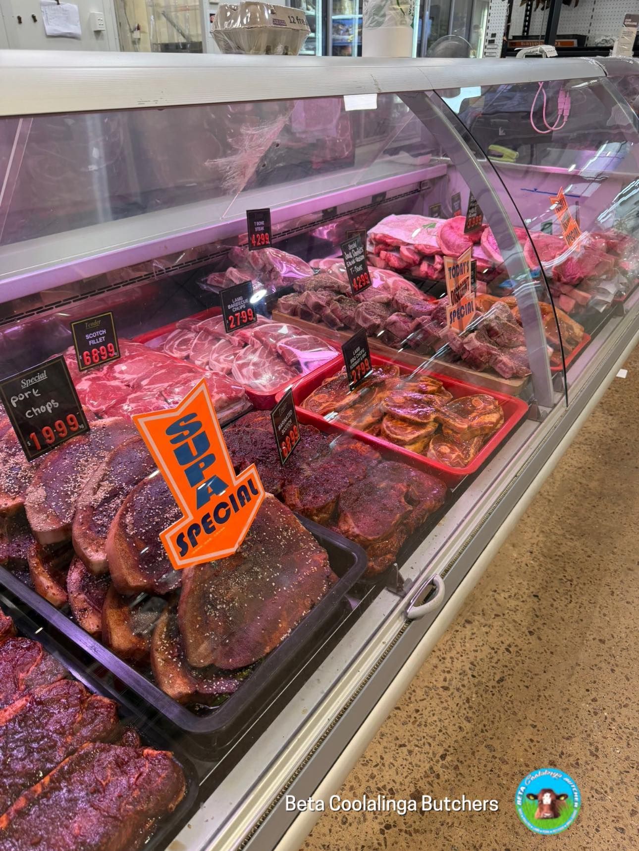 A refrigerated butcher's display case filled with various cuts of raw beef, some labeled 