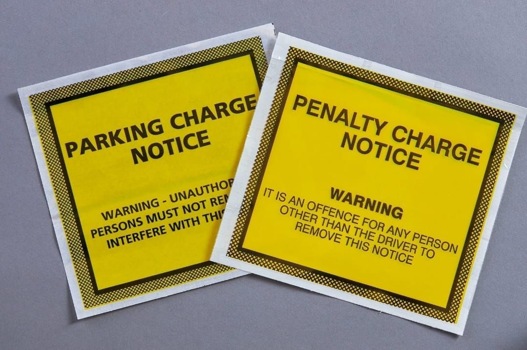 Two yellow parking and penalty charge notice stickers on a gray background.
