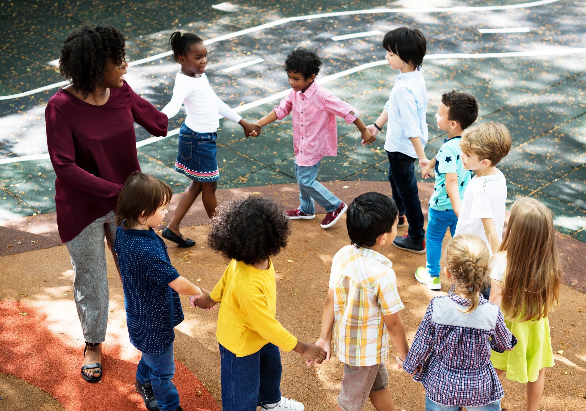 A group of children are holding hands in a circle with a teacher.