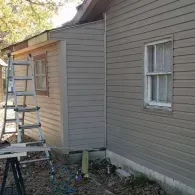 A multi-story aluminum extension ladder leaning against the exterior of a house with tan siding and a window.