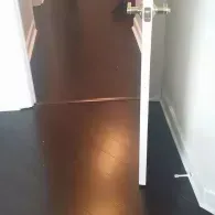 A white door with a silver handle stands slightly open, separating a dark brown wood floor from a dark grey floor area.