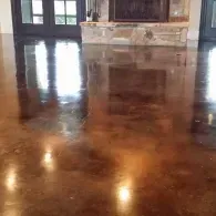 A highly polished, glossy brown concrete floor reflecting light and the surrounding room, with a stone fireplace in back.