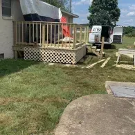 A wooden deck under construction with lattice skirting attached to the side of a house, with a work van parked nearby.