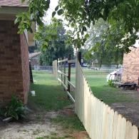 A wooden privacy fence under construction, extending from a brick house into a grassy residential yard.