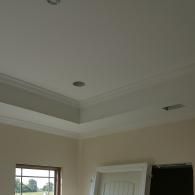 A corner view of a room with a beige wall, a white window, and a multi-tiered tray ceiling with crown molding.