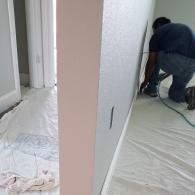 A person in a blue shirt kneels on a drop cloth to install electrical wiring in an unfinished interior wall.