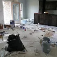 A messy construction site in a home featuring a doorway, dark kitchen cabinets, and debris scattered across the floor.