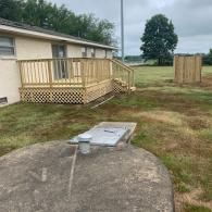 A beige house features a new wooden deck with lattice skirting, beside a concrete septic tank lid and a wooden enclosure.