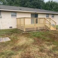 A newly constructed light wood deck with lattice skirting and a staircase, attached to the back of a light-colored home.