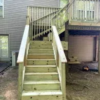 A newly built set of wooden stairs leading up to an elevated backyard deck.