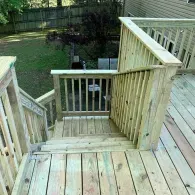 A wooden deck staircase with railing, looking down toward a grassy backyard and fence.