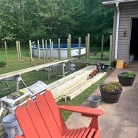 A red Adirondack chair in the foreground overlooks a backyard deck under construction near an above-ground swimming pool.