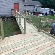 A newly constructed wooden wheelchair ramp with railings leading up to the red front door of a residential home.