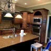 A kitchen island with a double sink and paper towel roll sits before dark wood cabinetry, stainless appliances, and island.