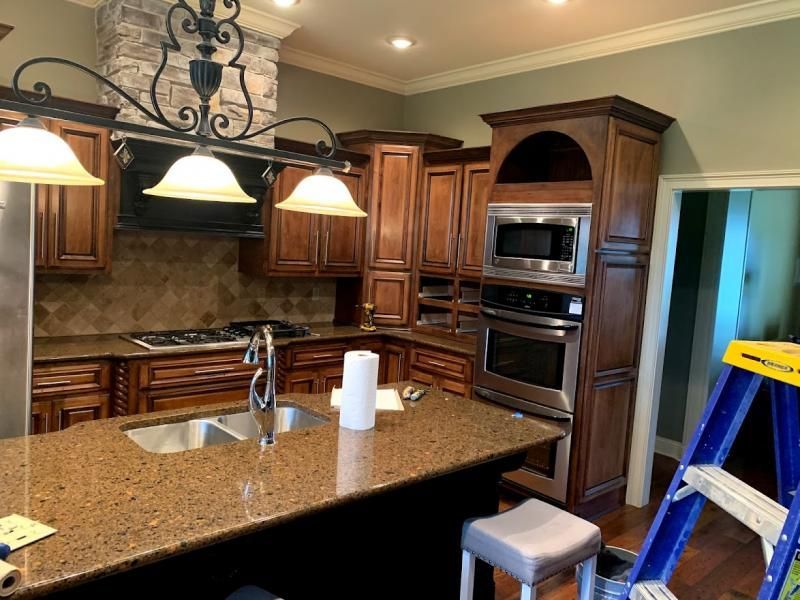 A kitchen with dark wood cabinets, brown granite countertops, an island with a sink, and stainless steel appliances.
