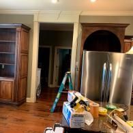 A kitchen remodel in progress showing a wooden bookshelf, a stainless steel refrigerator, and a ladder in the doorway.