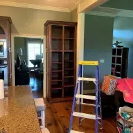 A tall, wooden, empty bookshelf stands in a room with hardwood floors, next to a blue ladder and a granite countertop.