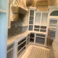 A kitchen under construction featuring white custom cabinetry, a large vent hood, and protective plastic covering surfaces.