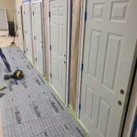 A hallway under construction with a row of newly installed white, six-panel doors and floor protection paper.