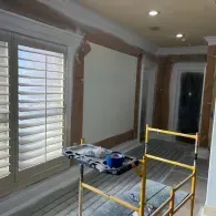 An interior view of a room under renovation featuring scaffolding, shutters on the left, and a doorway on the right.