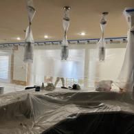 A room undergoing renovation, with pendant lights and surfaces covered in protective plastic sheeting.