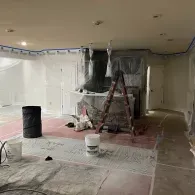 An interior room under renovation with protective plastic covering walls and a step ladder centered in the space.