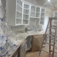A kitchen renovation in progress featuring newly painted white upper cabinets and protective coverings on the counters.