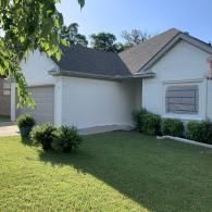 A single-story white house with a grey roof, a beige garage door, and a manicured lawn under a clear blue sky.