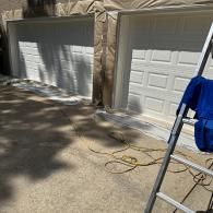Two white garage doors with brown protective masking paper around the frames, with a ladder in the foreground.