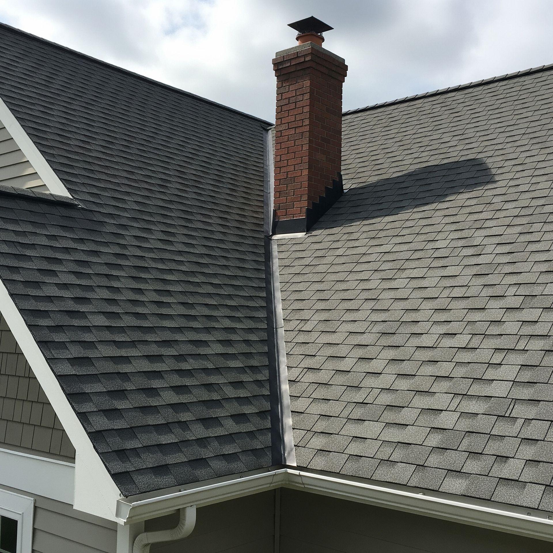 A residential roof in Delaware with gray asphalt shingles and a brick chimney.
