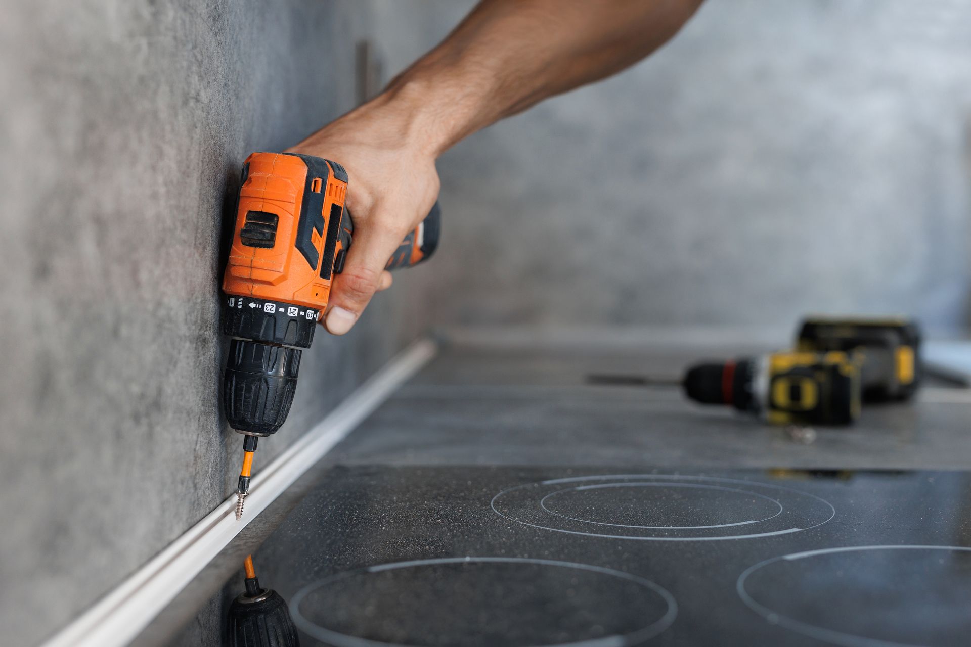A man is using a drill to install a counter top in a kitchen.