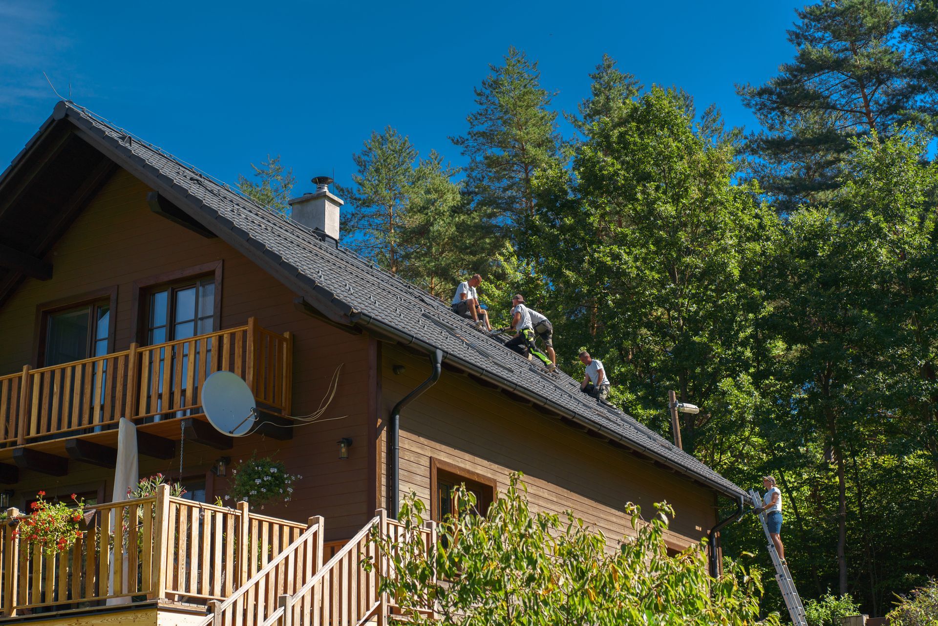A group of people are working on the roof of a house surrounded by trees.