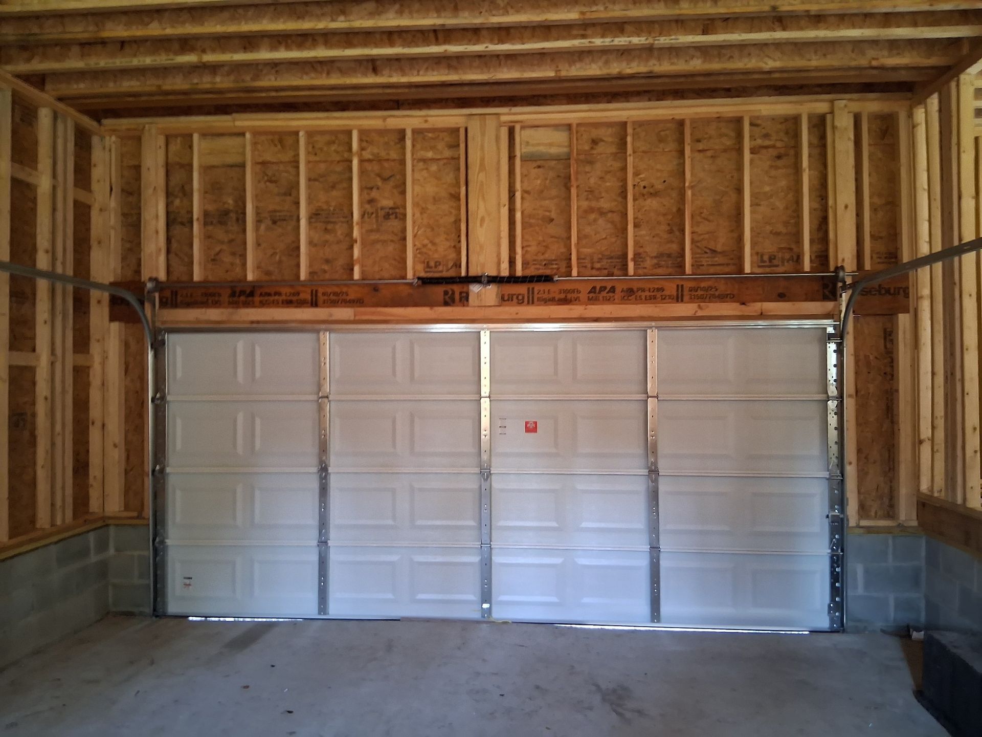 A white garage door is open in a garage under construction
