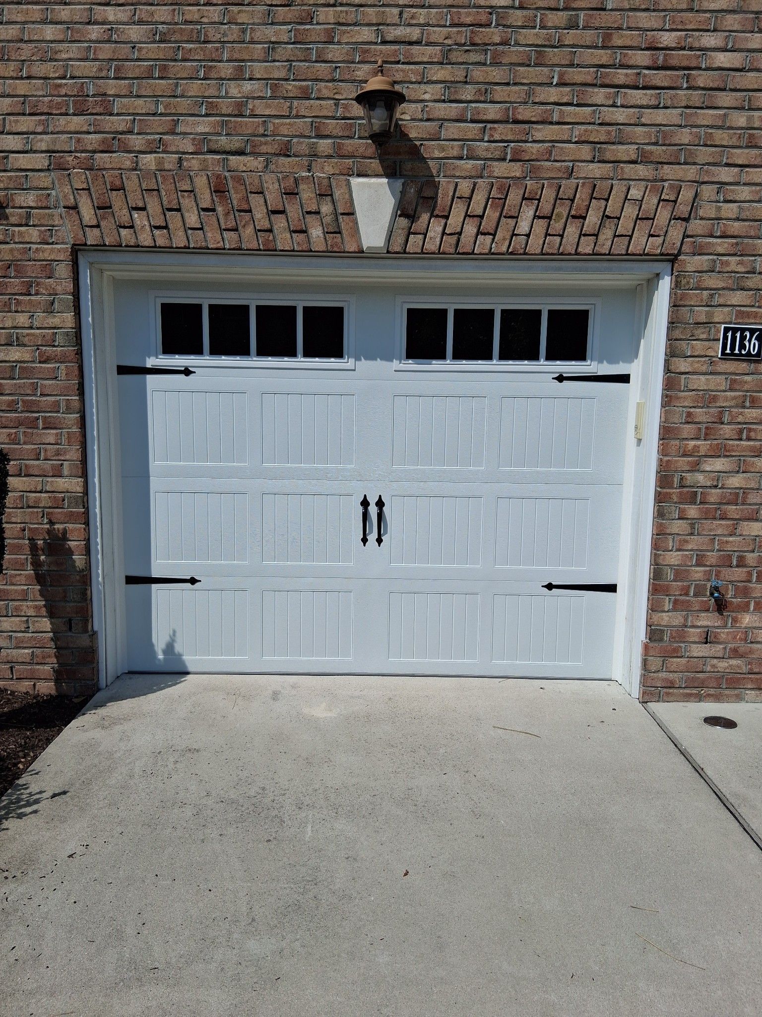 White garage door with black hardware, against a brick wall, with a concrete driveway.