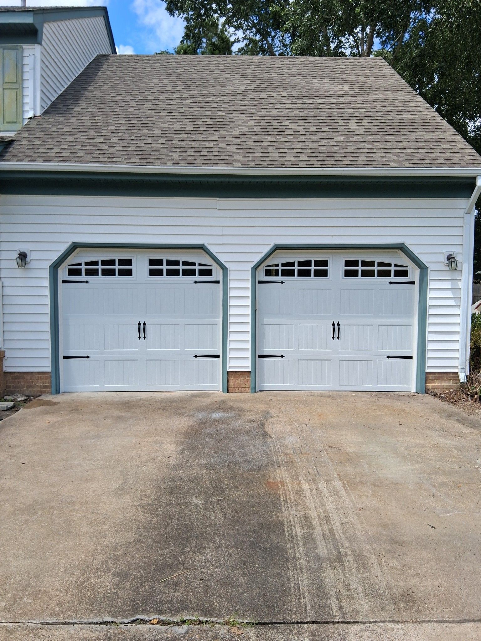 Two white garage doors on a house with a gray roof, concrete driveway.