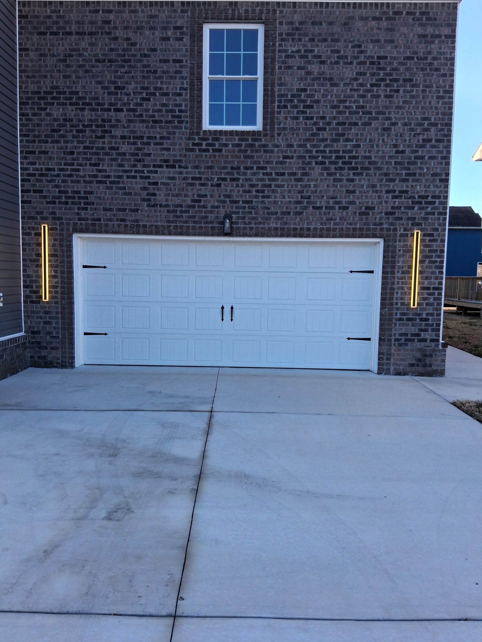 White garage door with black hardware, brick facade, concrete driveway.