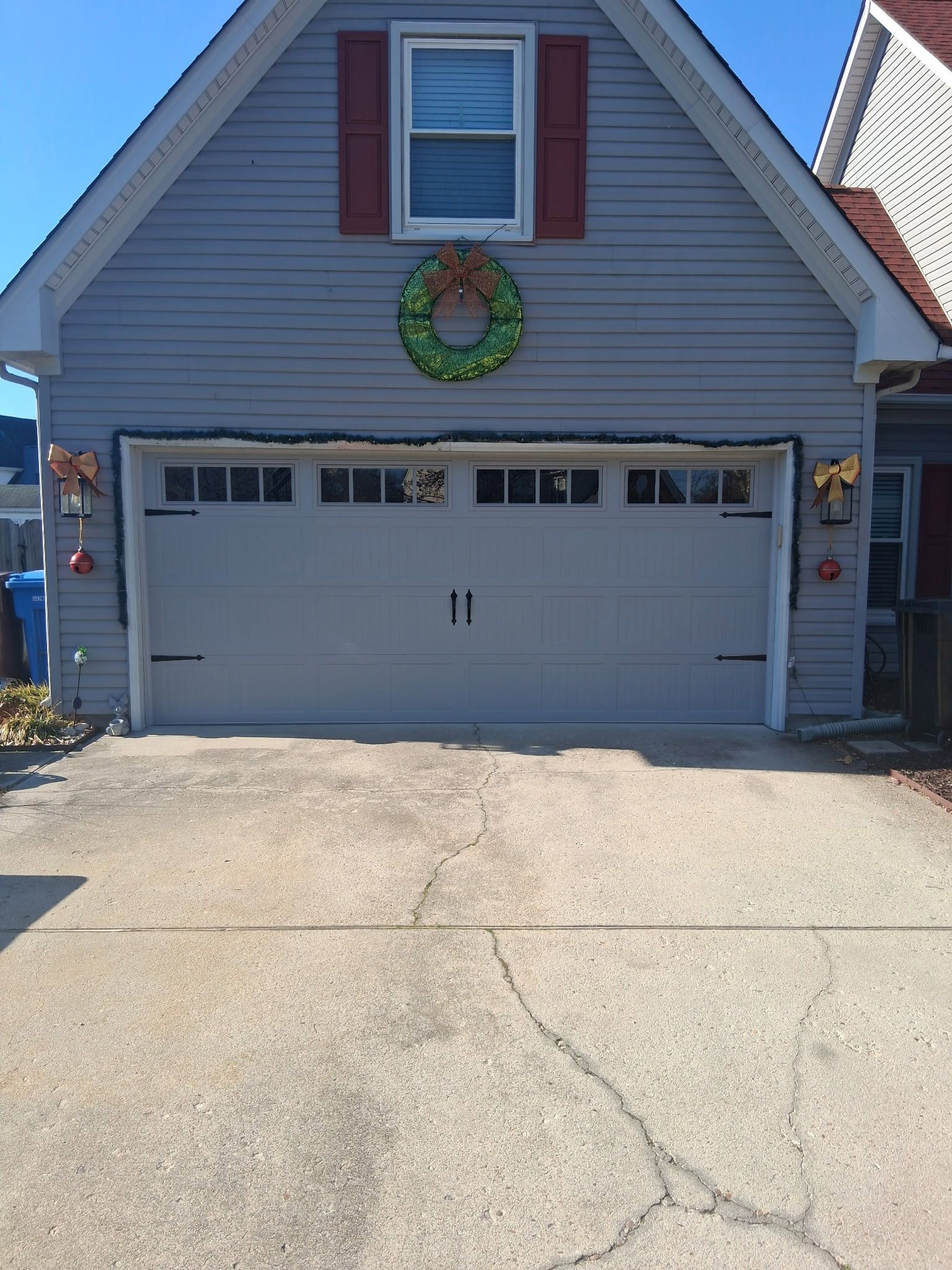 Gray garage door with a wreath and decorations, concrete driveway. Blue house.